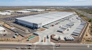 Aerial view of a large Los Angeles distribution center with numerous semi-trailers and trucks parked around the building, surrounded by parking lots and roadways in an industrial area.
